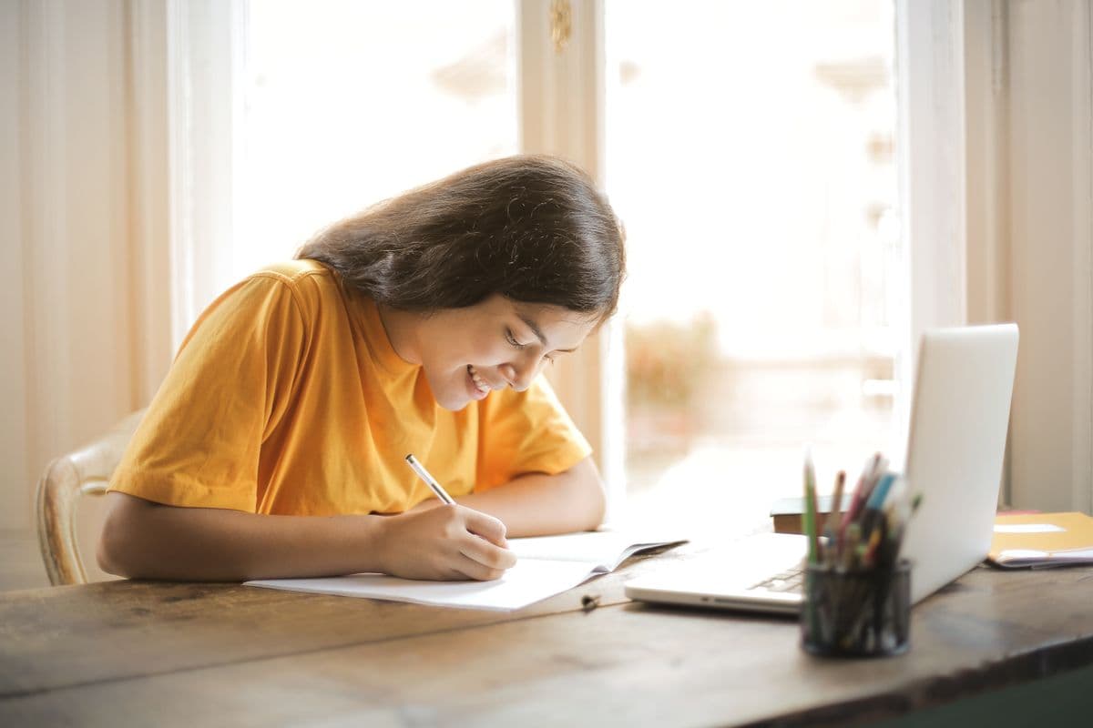 Jeune étudiante souriante, concentrée sur son ordinateur portable et ses notes