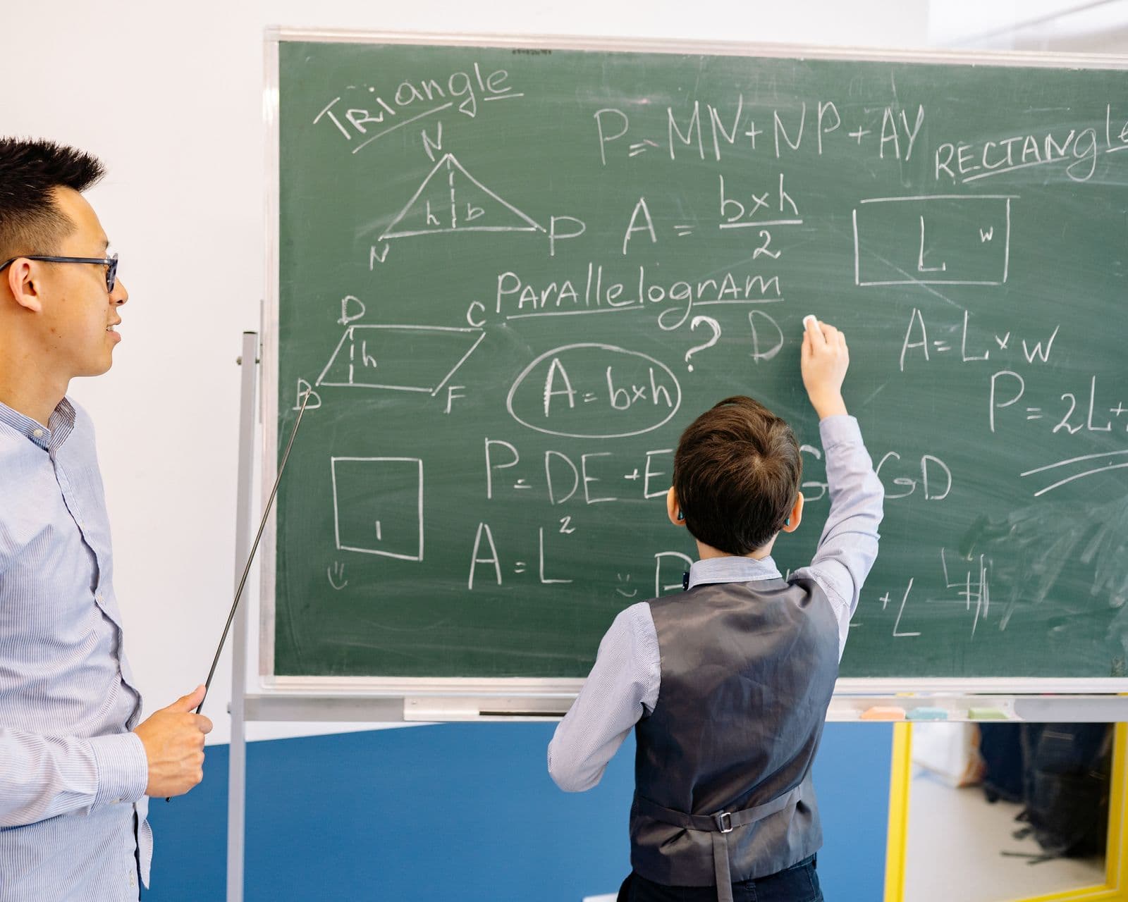 Professeur et élève échangeant devant un tableau couvert de figures de géométrie